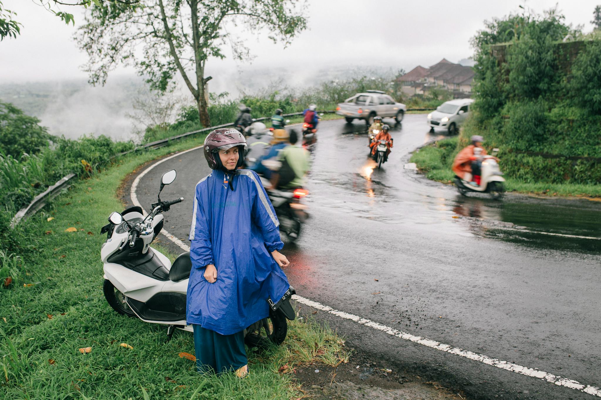Woman in raincoat on a mountain road with motorcycles during rain.
